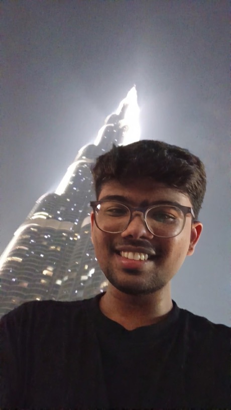 Himanshu smiling in front of the lit Burj Khalifa at night, Dubai